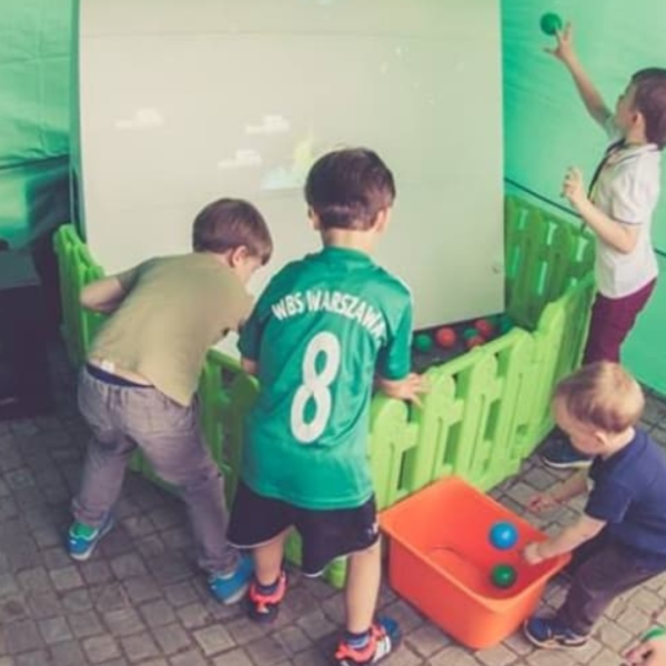 Dzieci bawiące się w interaktywnej grze rzutowej z piłkami w ogrodzonym kojcu.
