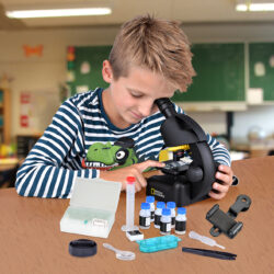 bresser-microscope-national-geographic-40-640x-04 Chłopiec w klasie szkolnej badający próbki pod mikroskopem National Geographic z zestawem akcesoriów laboratoryjnych.