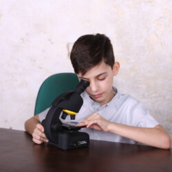bresser-microscope-national-geographic-40-640x-09 Chłopiec badający preparat pod mikroskopem National Geographic przy biurku z globusem i książkami.