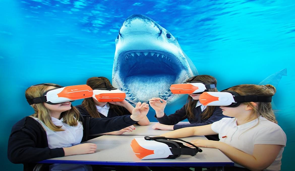 Uczniowie w goglach VR oglądają symulację podwodną z rekinem.